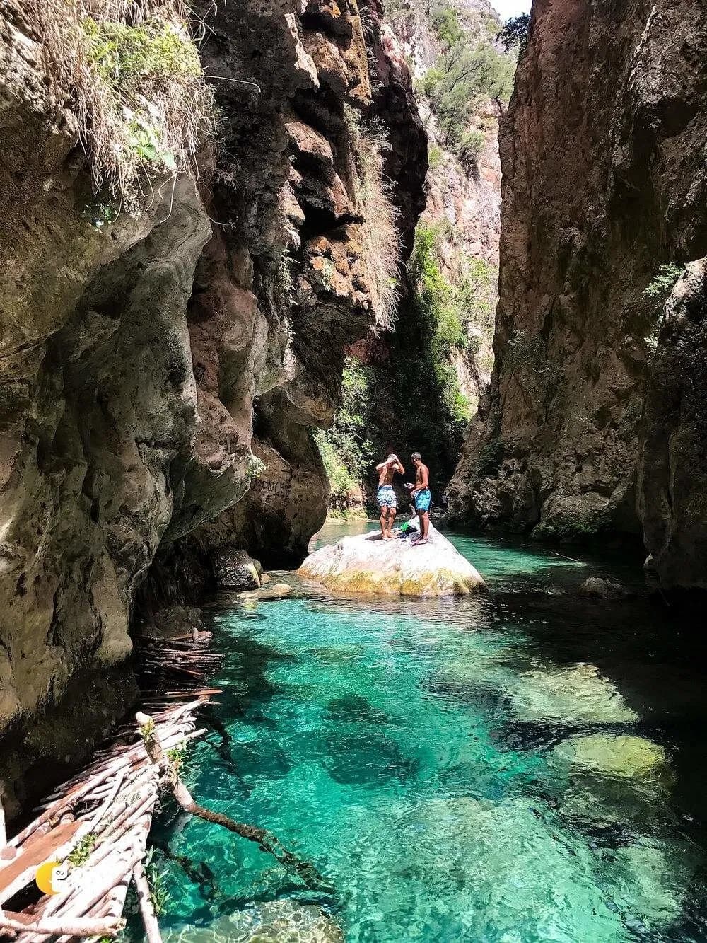 Two hikers on a rock above a turquoise pool in the Akchour gorge