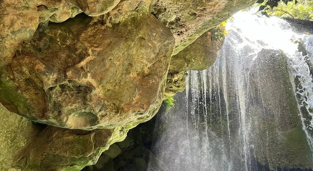 Waterfall flowing beneath a mossy rock overhang at Akchour