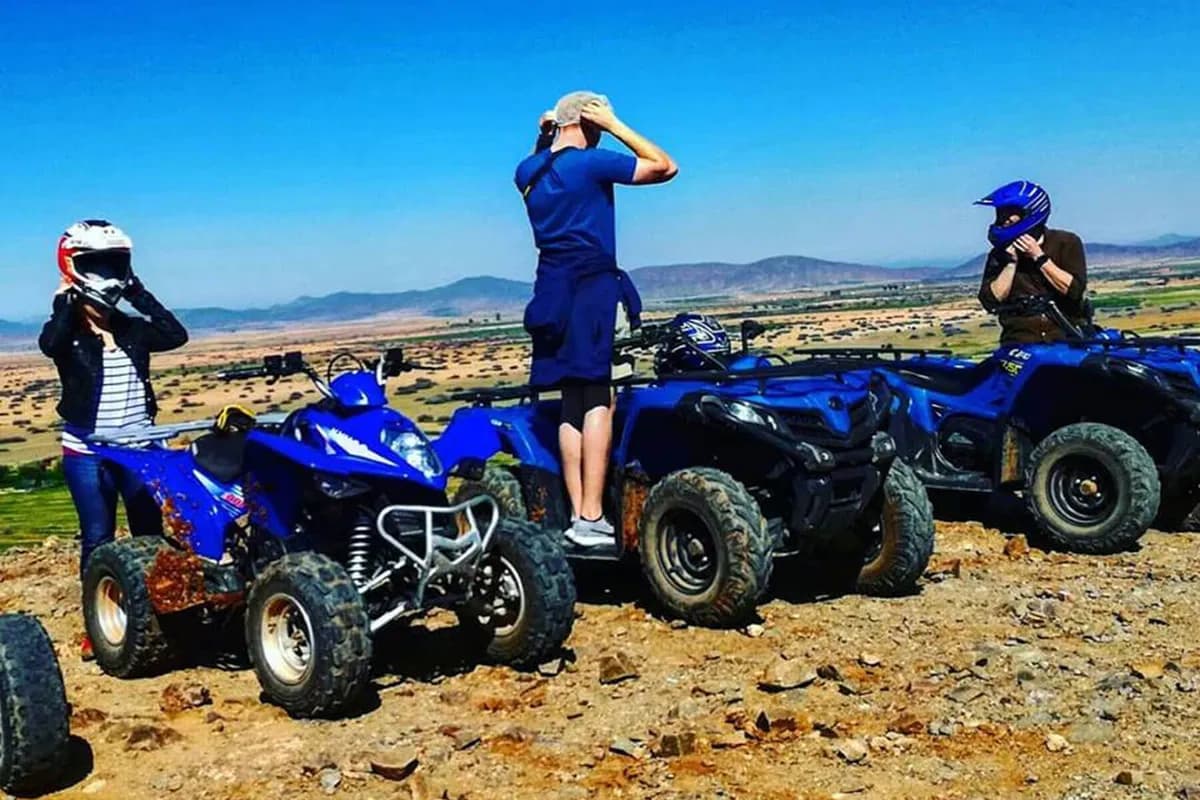 Riders putting on helmets beside blue quad bikes above farmland