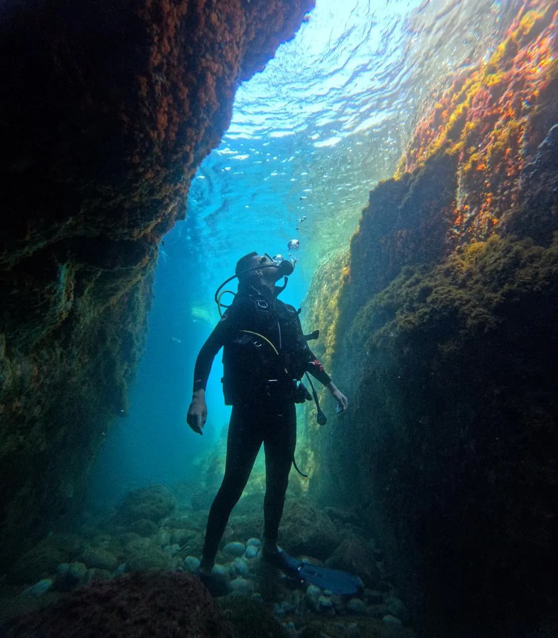 Scuba diver standing between rock walls in clear blue water